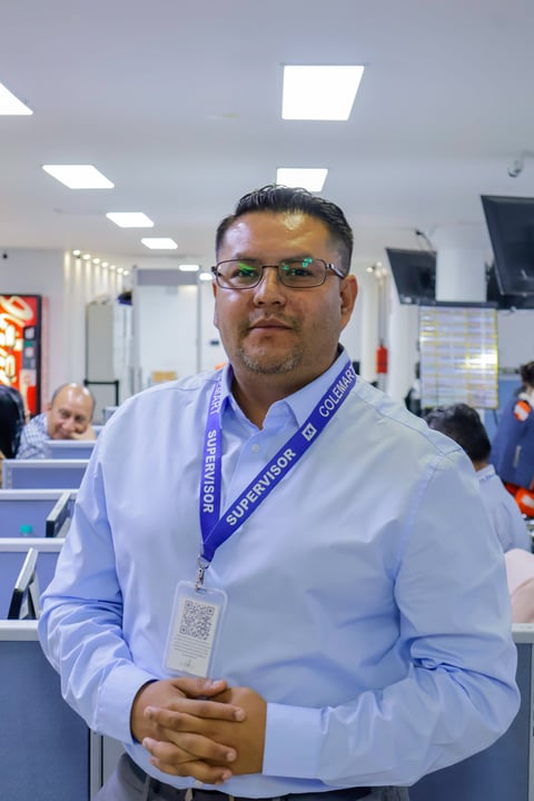 Man wearing blue shirt and glasses with supervisor lanyard standing in office environment