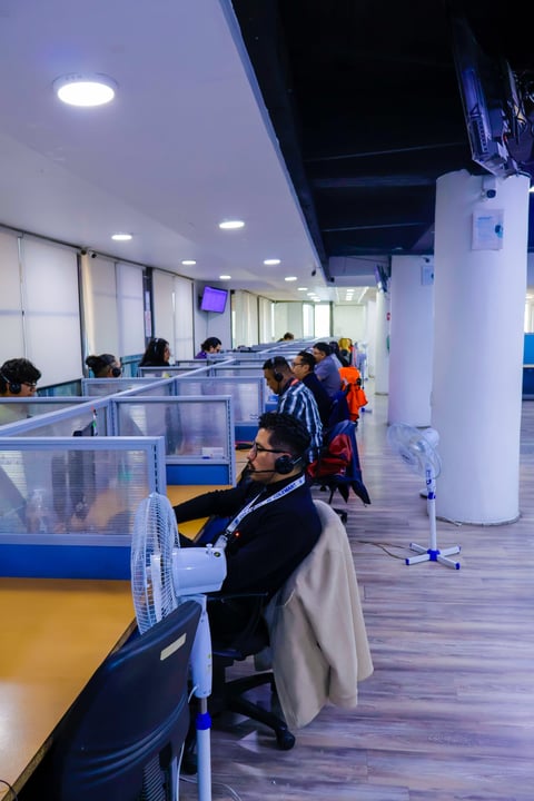 Modern office interior with multiple workers at blue and yellow desk partitions under bright LED ceiling lights