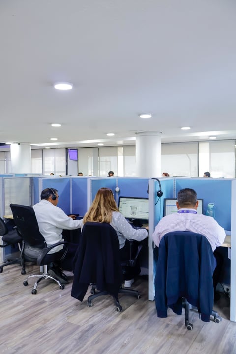 Open office workspace with employees working in blue-partitioned cubicles with computers and headsets