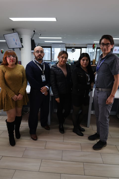 Five people standing in an office or corporate setting, wearing business casual attire and ID badges, posing for a group photo.